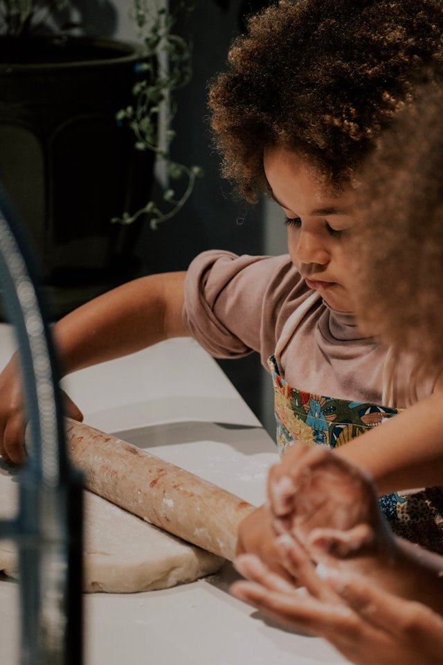 A child rolling dough with a parent's help