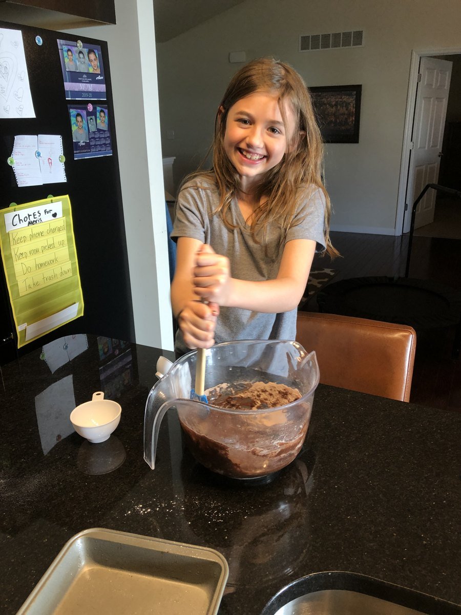 A young girl happily stirring brownie batter in the kitchen